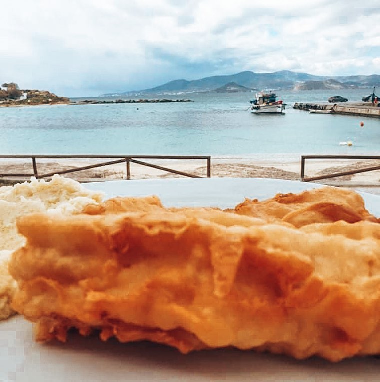 Outdoor dining at Gorgona Taverna with sea view, featuring fresh Greek salad, bread basket, and traditional dips against backdrop of turquoise Aegean Sea and boats